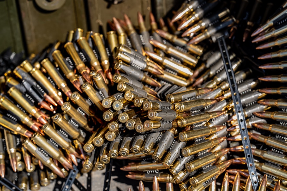Linked belt-fed machine gun ammunition and loaded magazines laid out in an ammo can at a private Texas range